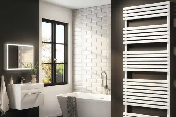 Modern bathroom featuring a freestanding white bath, wall-mounted vanity unit with illuminated mirror, and a tall white ladder-style heated towel rail against a dark accent wall